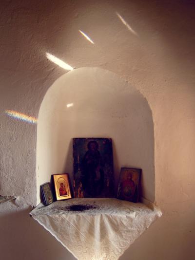 “On a top of a hill was where that small chapel was built. Abandoned by the faithful, lonely, with the view of the mountain Pelion ricing on the right and smaller hills laying underneath it, on the left, reaching the Pagasitikós gulf. Built there, exposed to the sunlight from the beginning of the day until the end, overflowed by all these lights and having the north wind coming from the mountain rubbing its cracked walls, it was the chapel of Agios-Athonas.
Standing there, with a timeless world of light and life around me, colourful and rich in smells and sounds, that didn’t even notice my existence, made me feel powerless, invisible, facing a big world with its dominant, natural flow of life and death.  A small glimpse of fear would appear, crawling slowly from each corner of my body to my heart, telling me that I’m nothing more than a part of that flow, nothing more than life and death. I would look up, search for Him in the endless blue sky but I could never meet His figure with my eyes because He was nowhere, yet, He was everywhere. Sometimes, I would open the door of the chapel and get inside the small, dark space closing the door behind me. It was very quiet there, I could feel the quietness. The only noise was the wind trying to get inside from a small hole on the roof, like a whistle, a dimmed song of an invisible force that for some reason would make the quietness more notable.  Then, I would light a candle in front of the icon of the holy, of Agios-Athonas and sit on a chair looking at that small source of light dancing with its own death. Being as powerful and vivid as the light of the sun outside, it felt like I brought a drop of this light inside, creating this flame, giving birth to the holy spirit inside the chapel.”